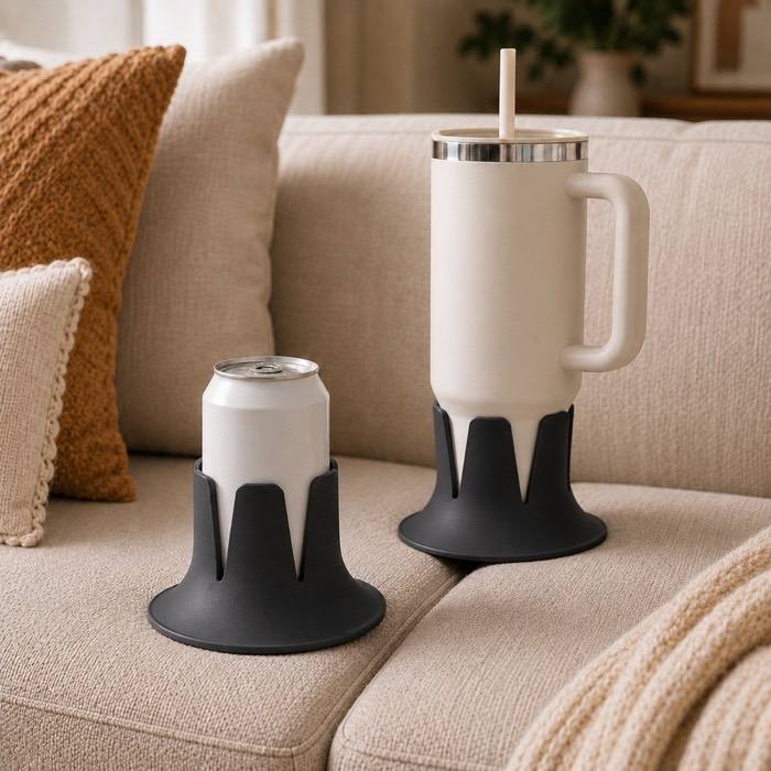 A can and a large tumbler, each seated in a charcoal drink holder, on a couch cushion.